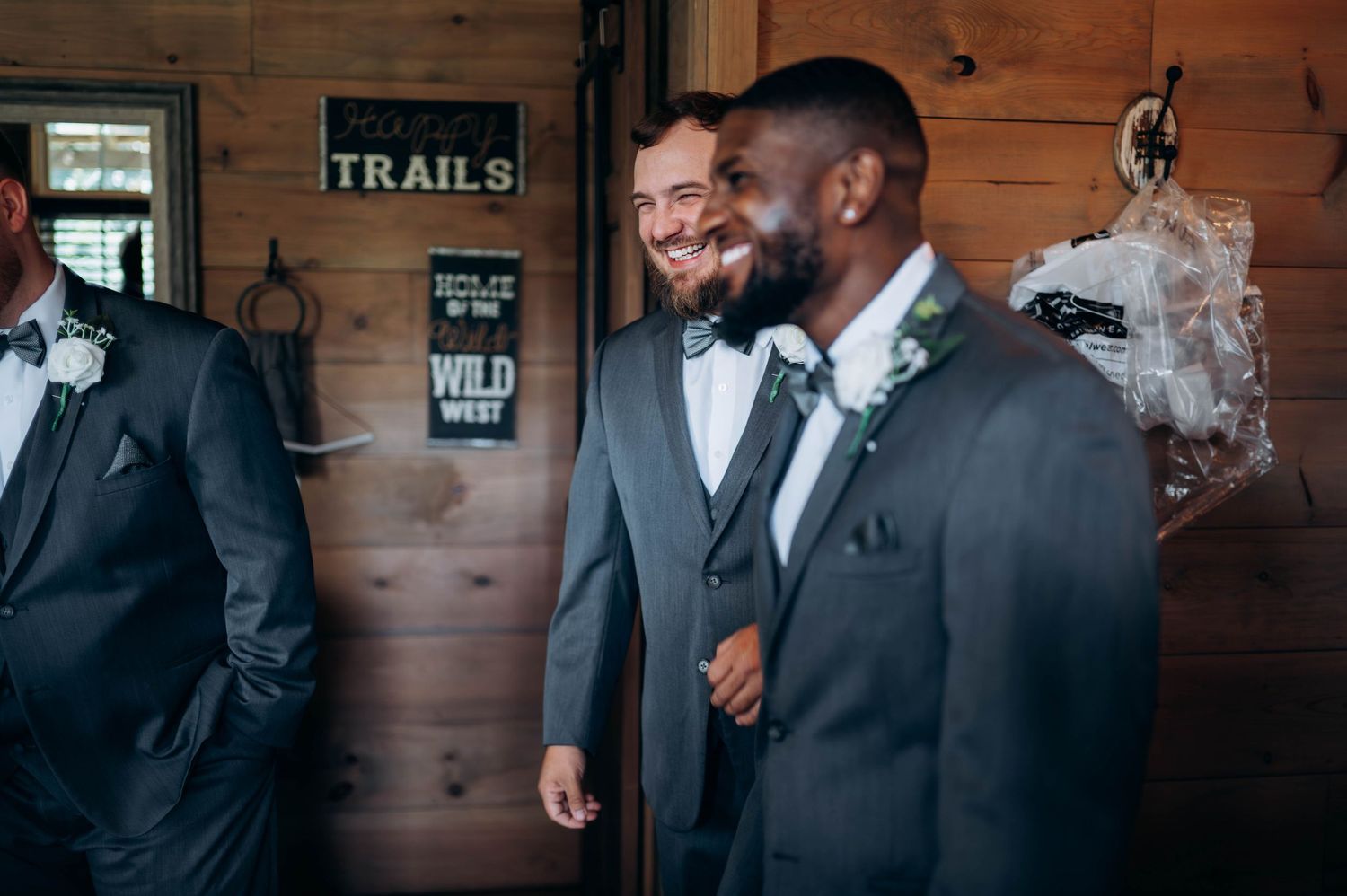 Groomsmen in formal attire sharing moments in a wooden-paneled room with rustic decor.