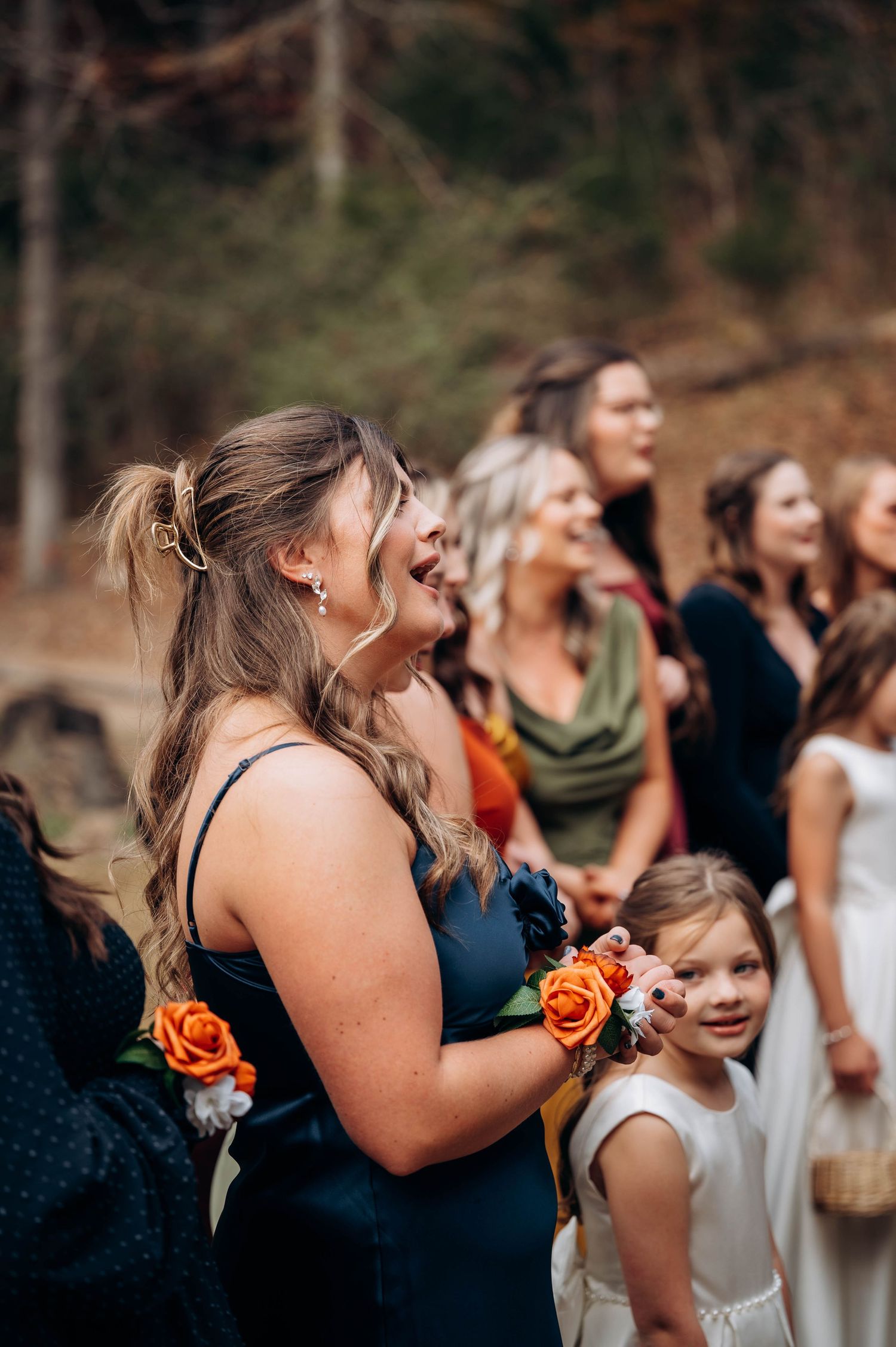 Bridesmaids in navy dresses share emotional reactions during wedding ceremony in autumn setting.