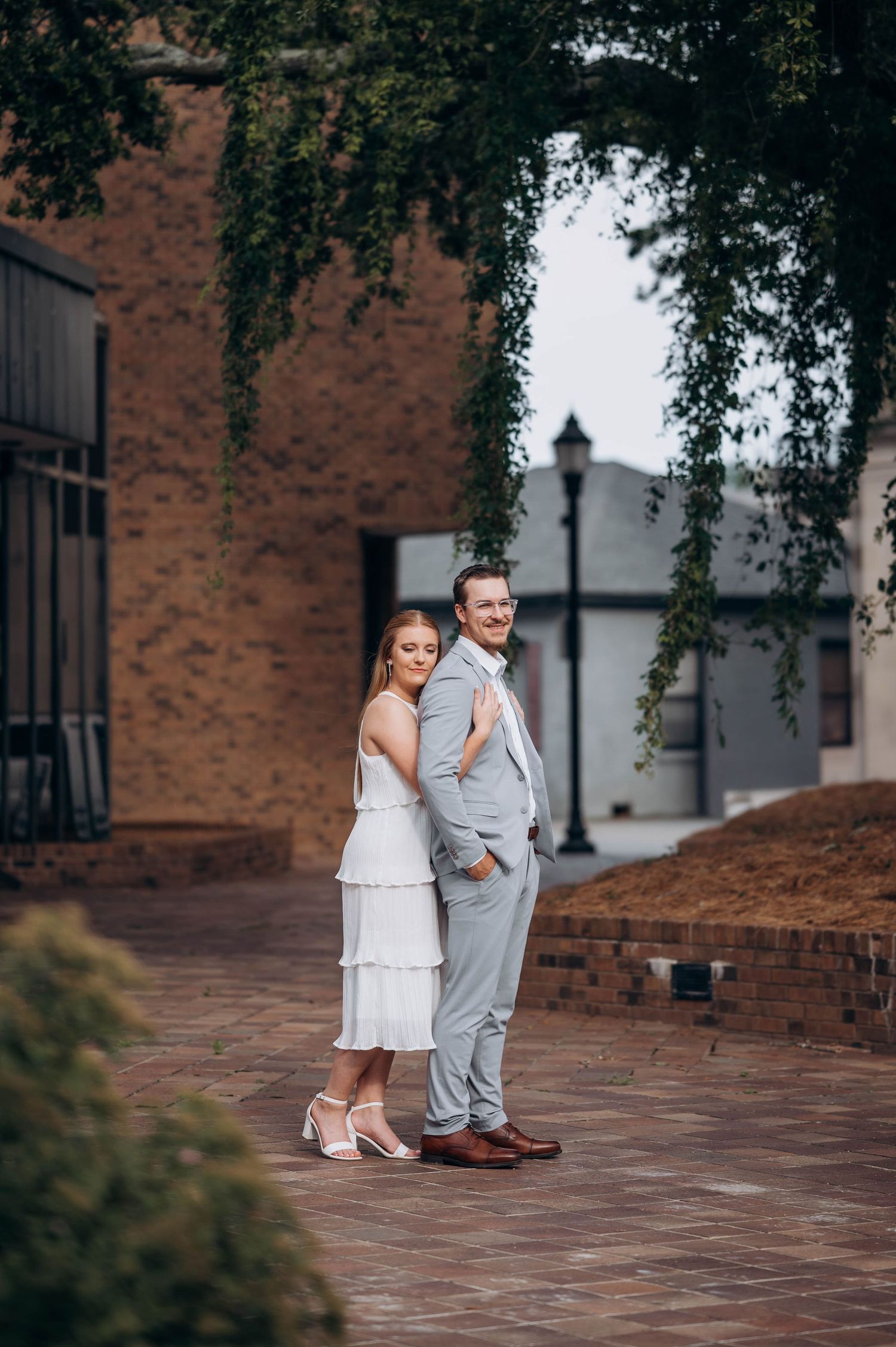 A couple stands close together on a brick patio surrounded by historic architecture.