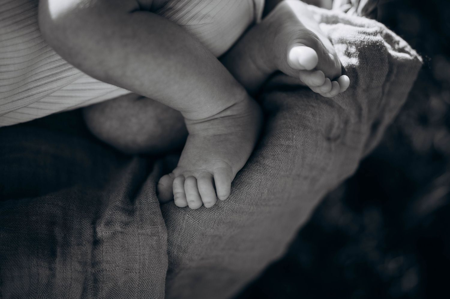 Close-up of hands gently cradling a newborn baby wrapped in soft fabric.