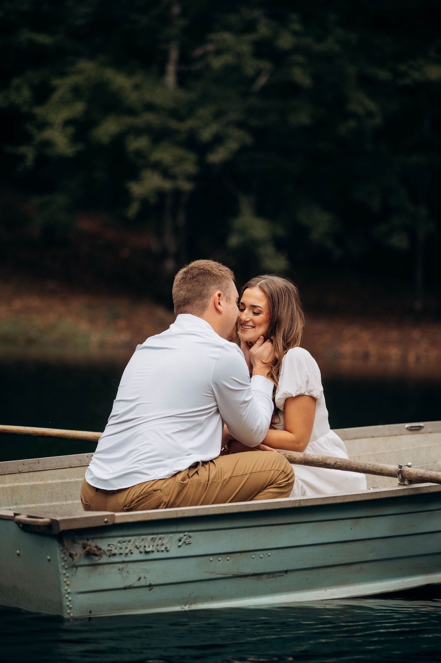 Couple dressed in white and khaki share tender moments while sitting in a rowboat.