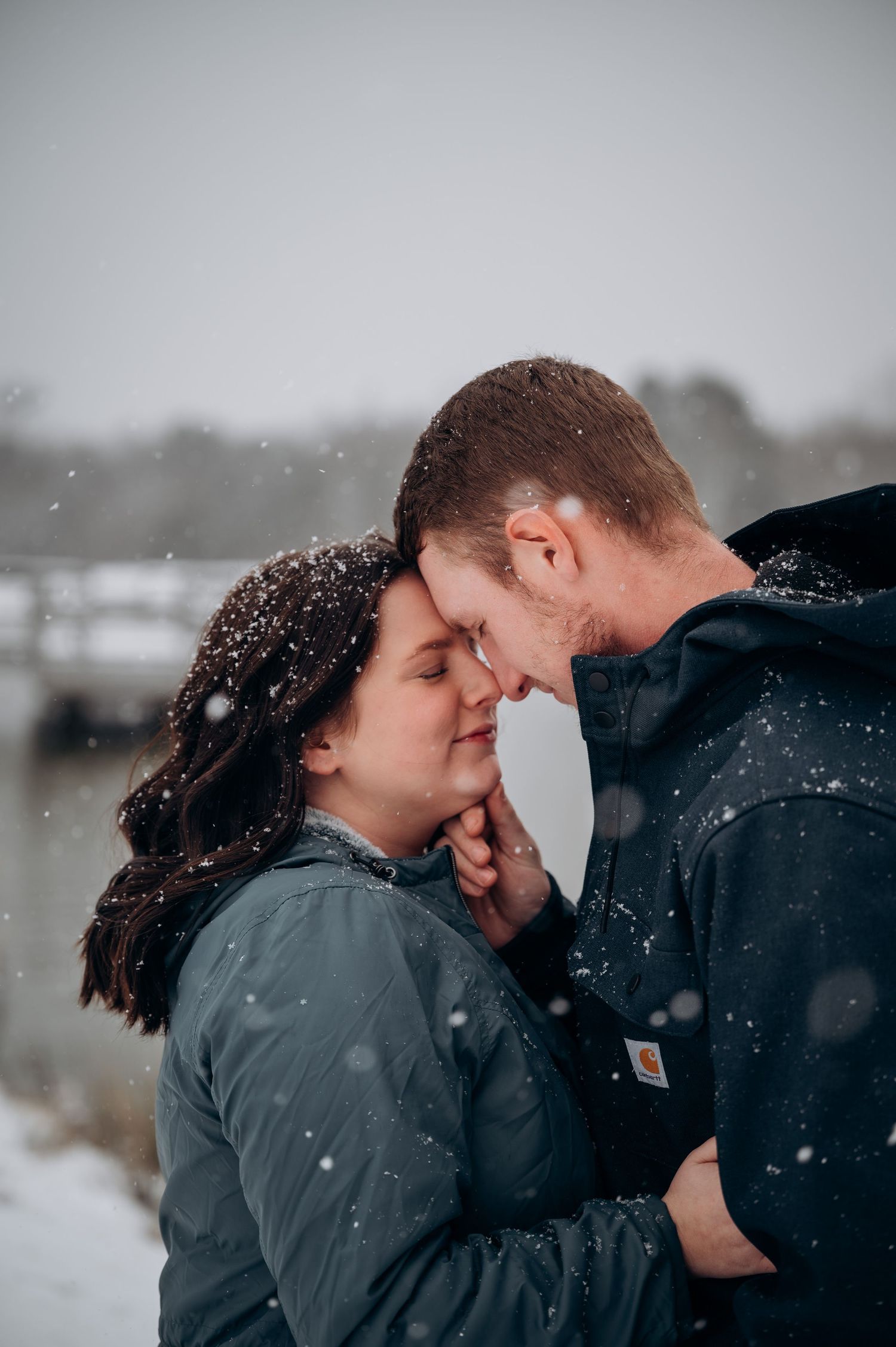 Close-up shot of two people sharing an intimate moment during a gentle snowfall on a winter day.