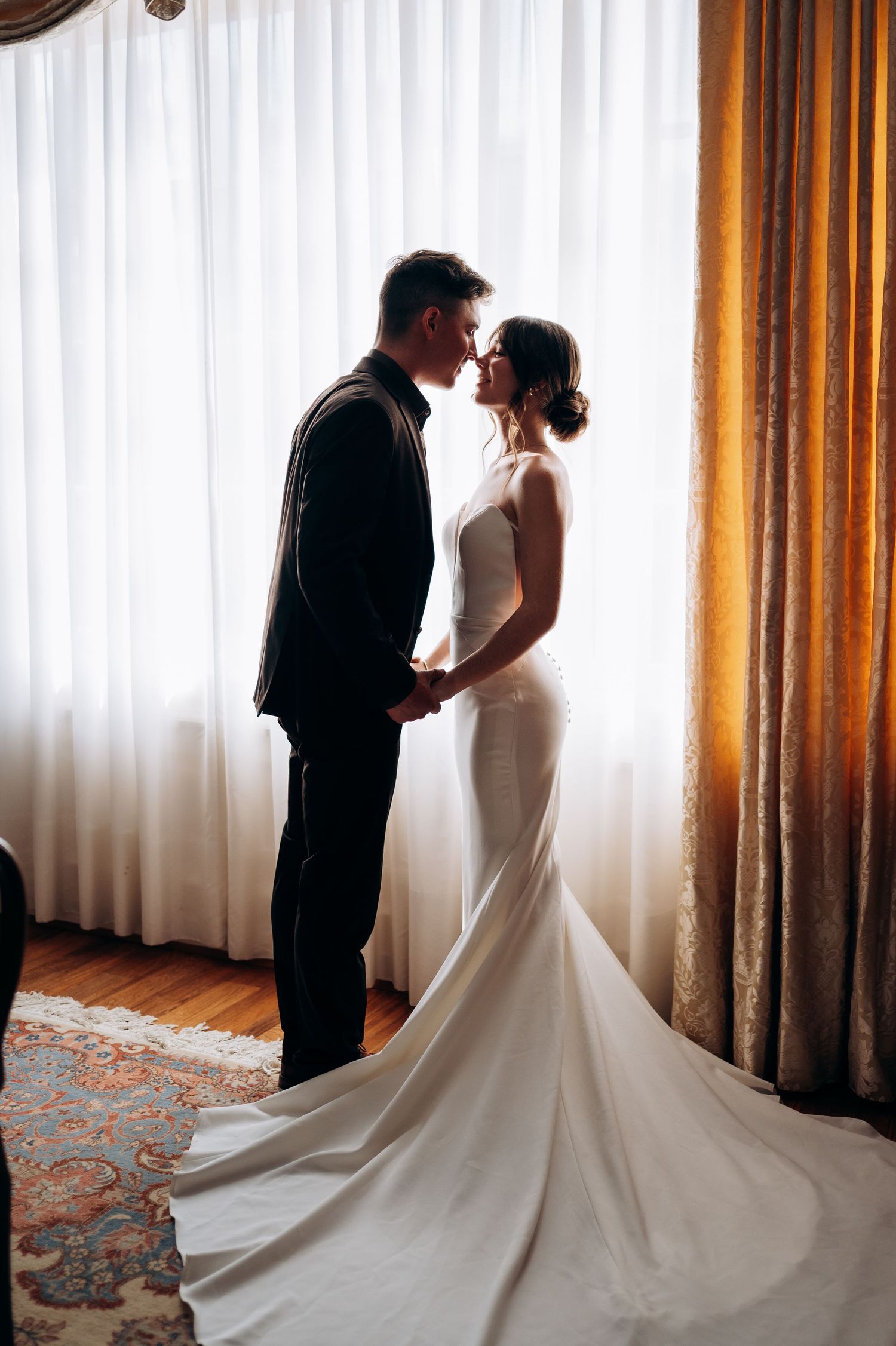 Wedding couple in silhouette against window light with dramatic white gown train.
