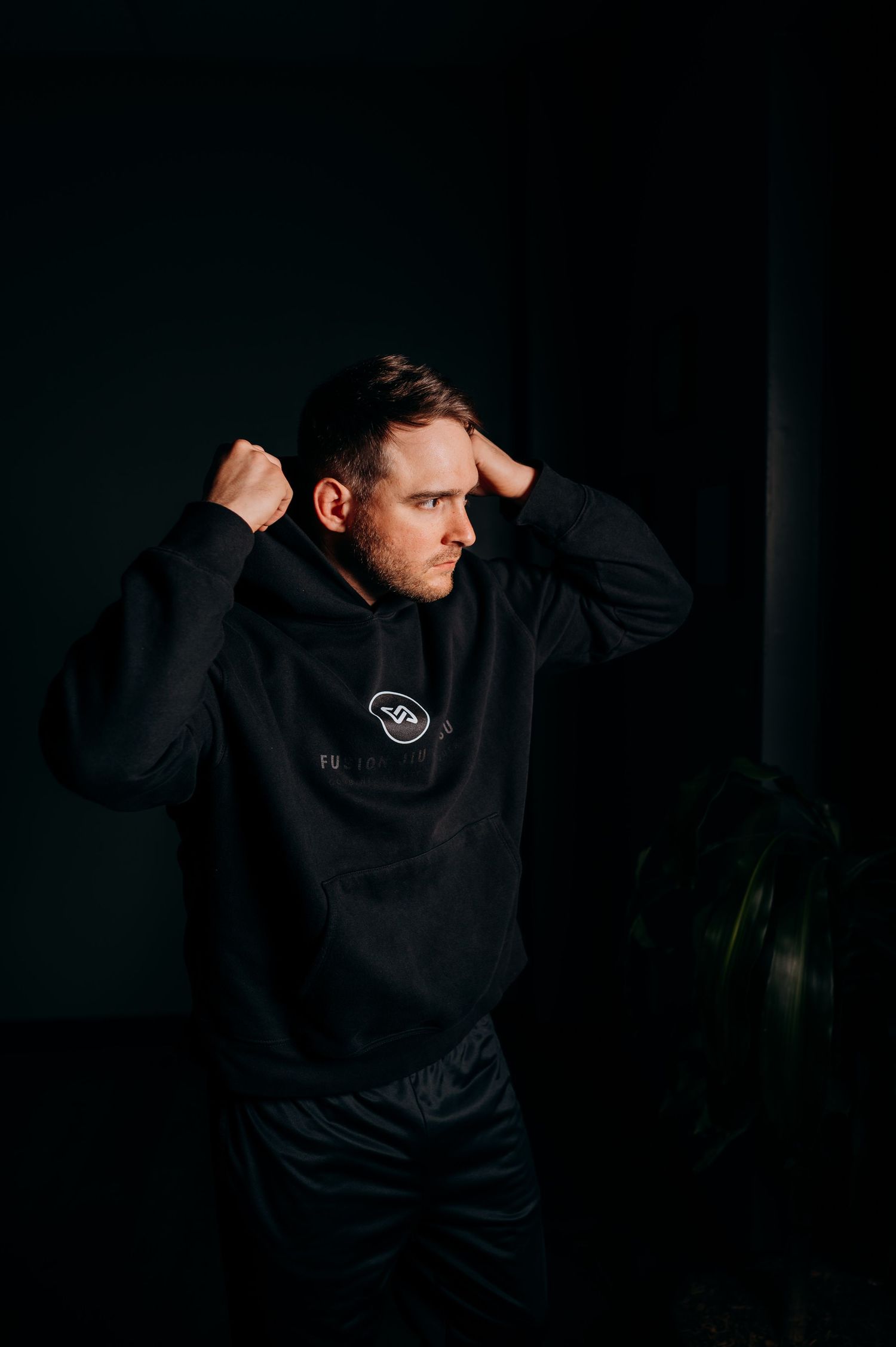 Athletic figure in black hoodie shown in dramatic low-light profile against dark background.