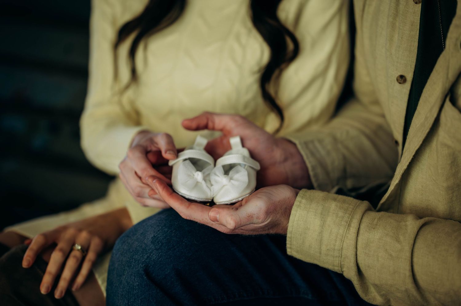 Couple holding tiny white baby booties together, announcing pregnancy.
