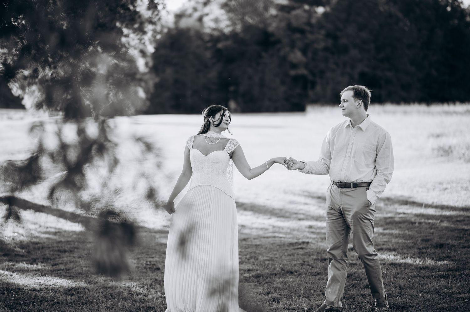 Black and white photo of a couple holding hands while walking through a lush green park on their wedding day.