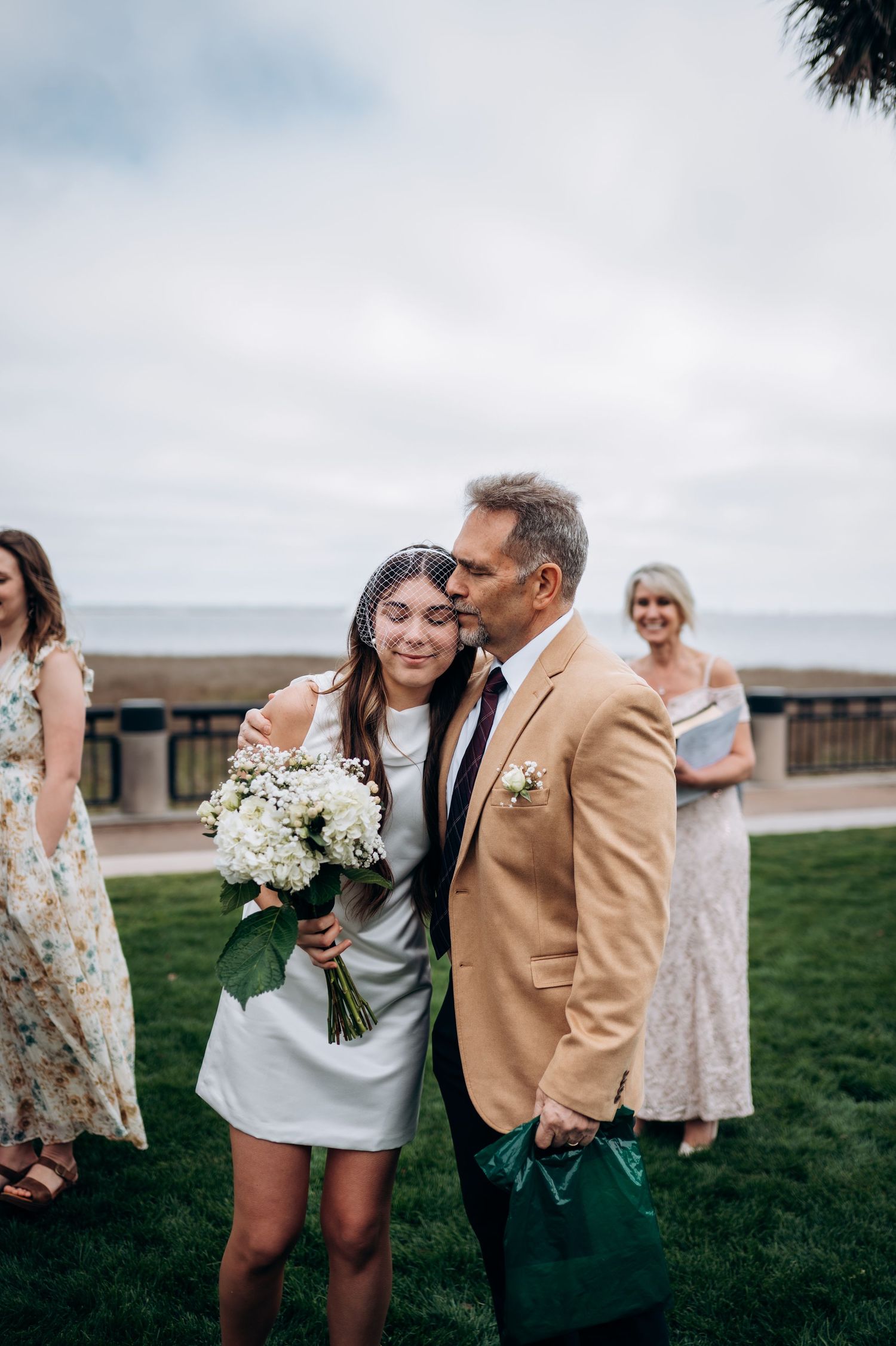 A couple shares a joyful moment during a wedding celebration on a grassy lawn by the ocean.