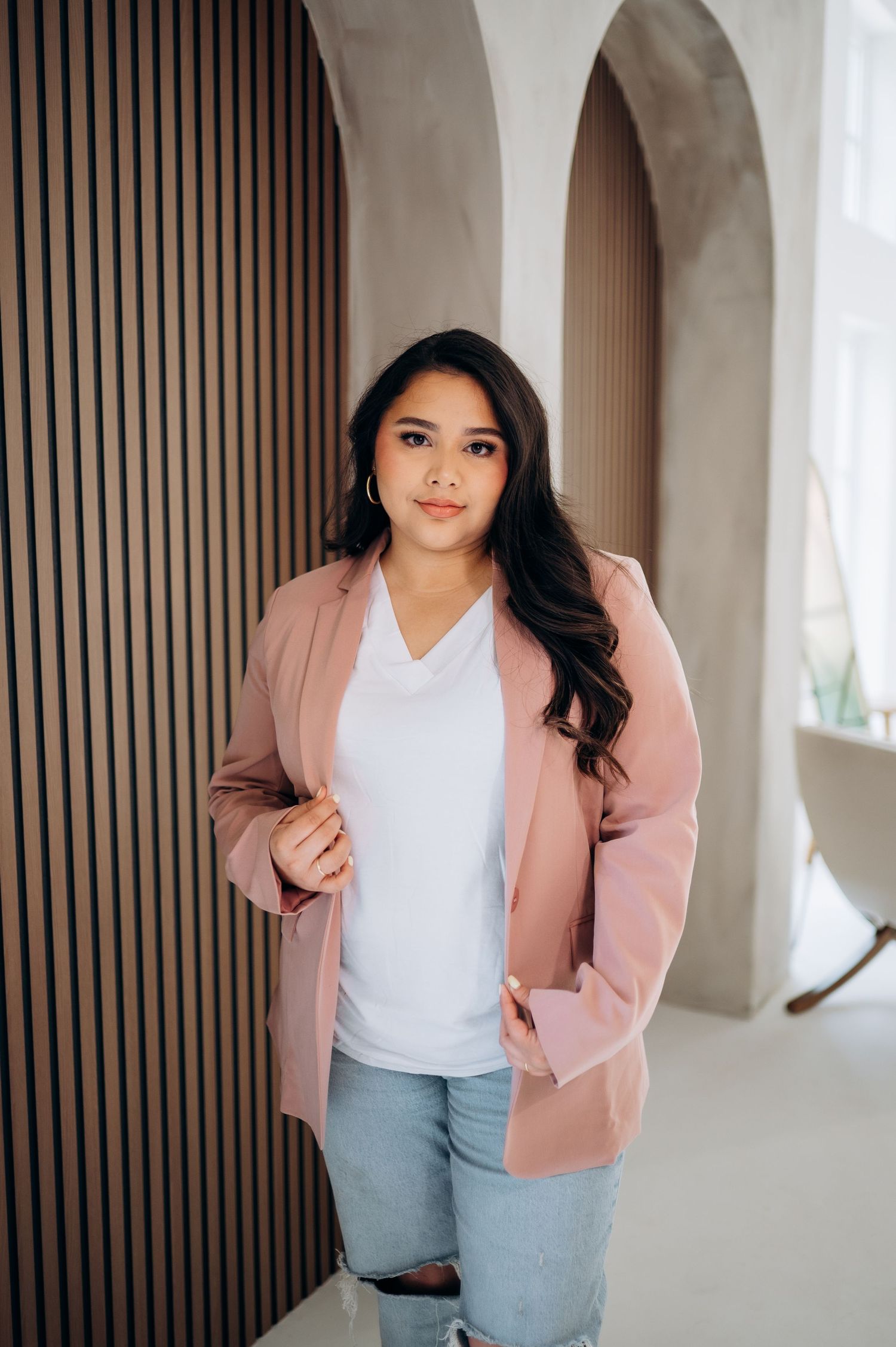 Woman in pink blazer and white top poses against a modern architectural background.