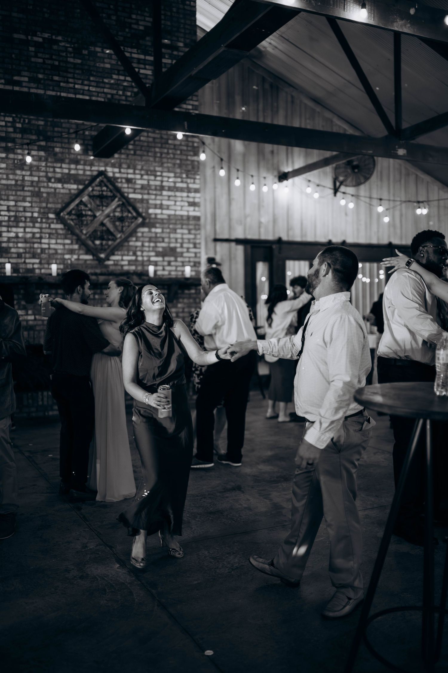 Black and white photo of wedding guests dancing in an industrial-style reception venue.