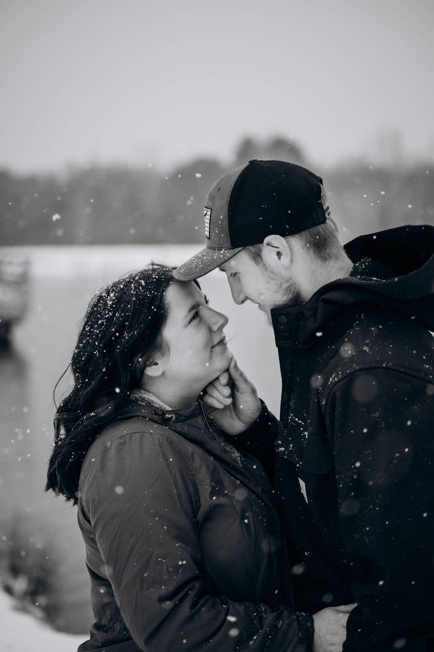 A romantic winter scene with a couple sharing an intimate moment as snowflakes fall around them in black and white.