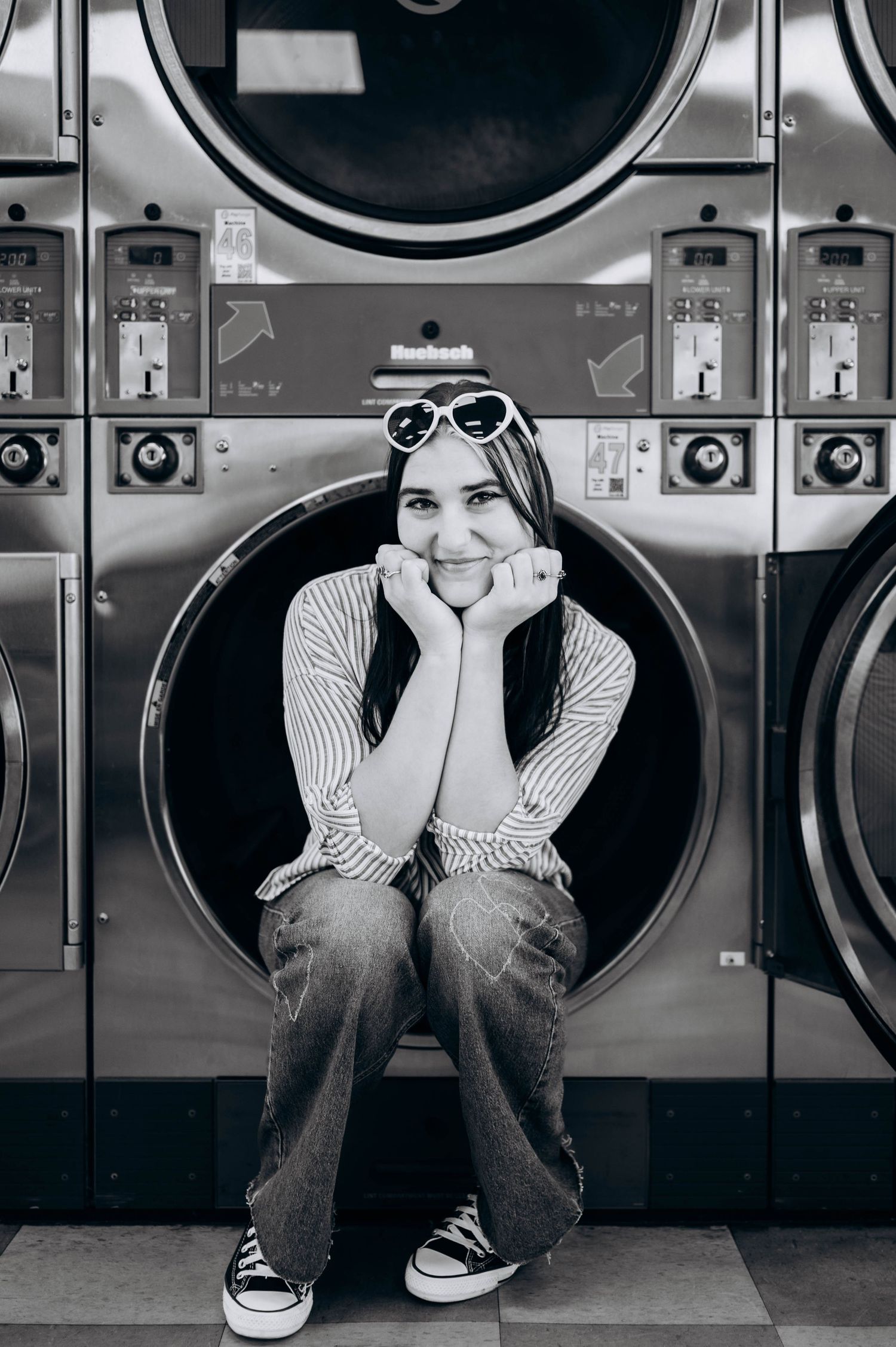 Monochrome series showing person in striped shirt and jeans sitting against industrial washing machines.