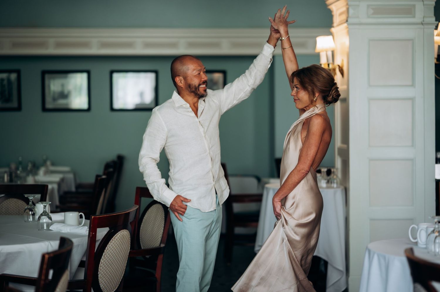 Romantic couple sharing a high-five dance moment in a stylish teal restaurant.