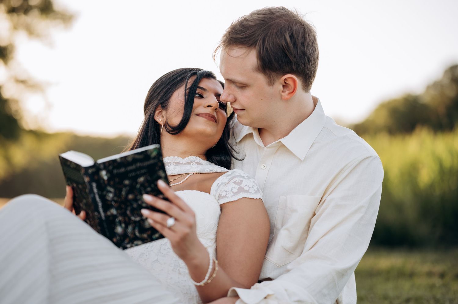 A couple in wedding attire sharing a romantic moment while reading a book together outdoors.