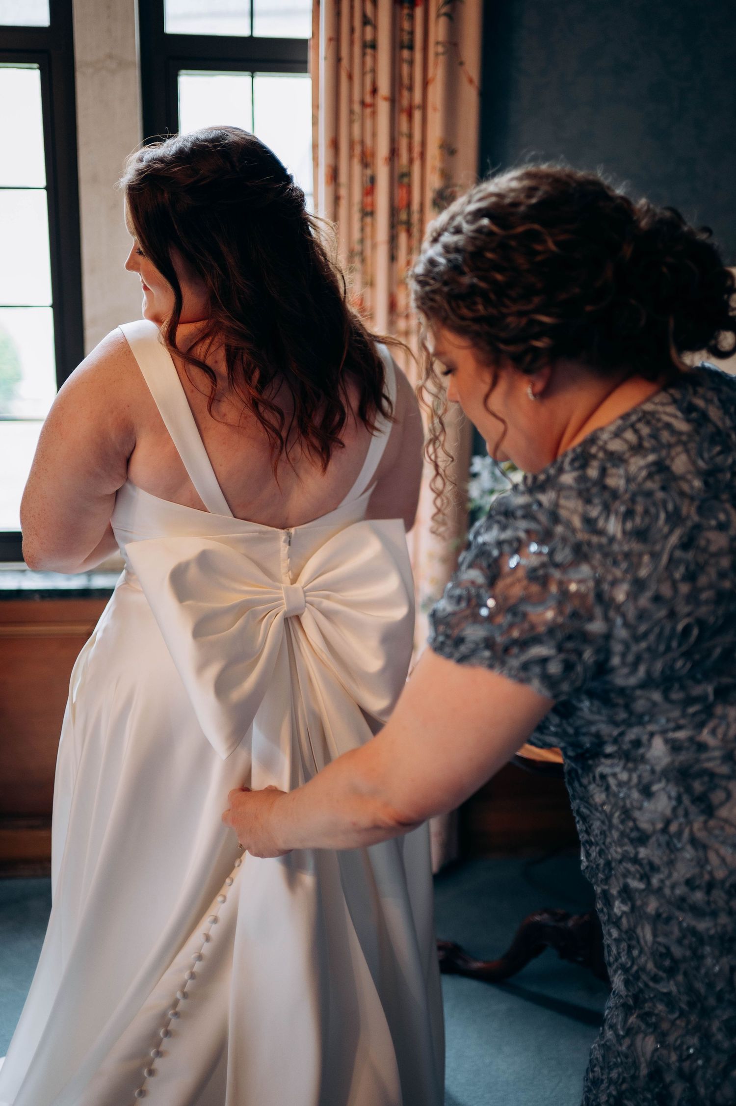 A close-up of a wedding dress bow detail being adjusted.