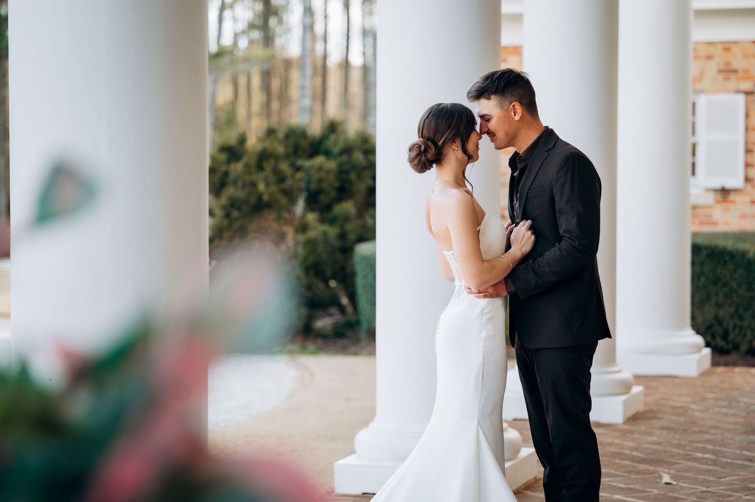 Wedding couple embracing between white columns outdoors at elegant venue.