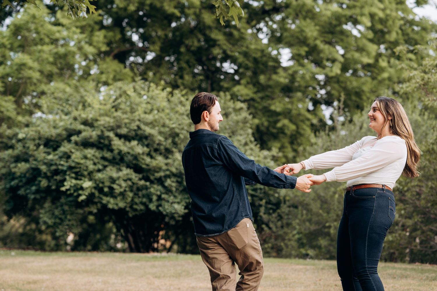 Couple playfully holding hands and spinning together on a green grassy park lawn.