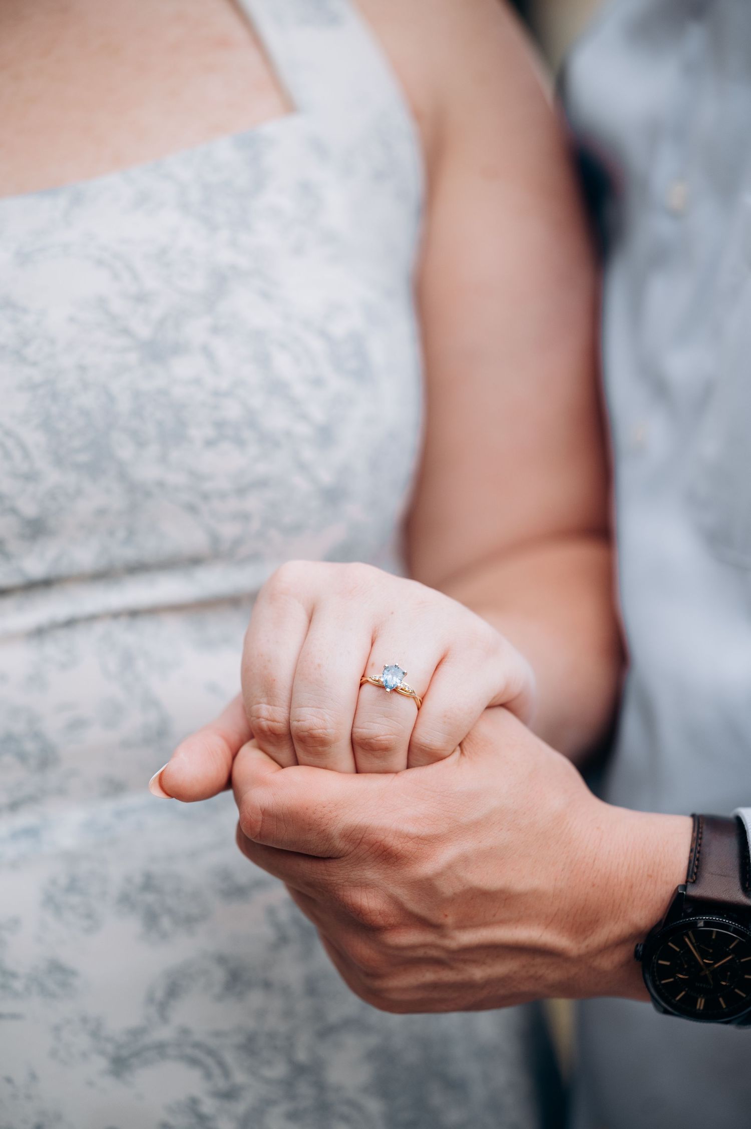 Close-up of woman's hand showing gold diamond engagement ring held by man wearing watch.