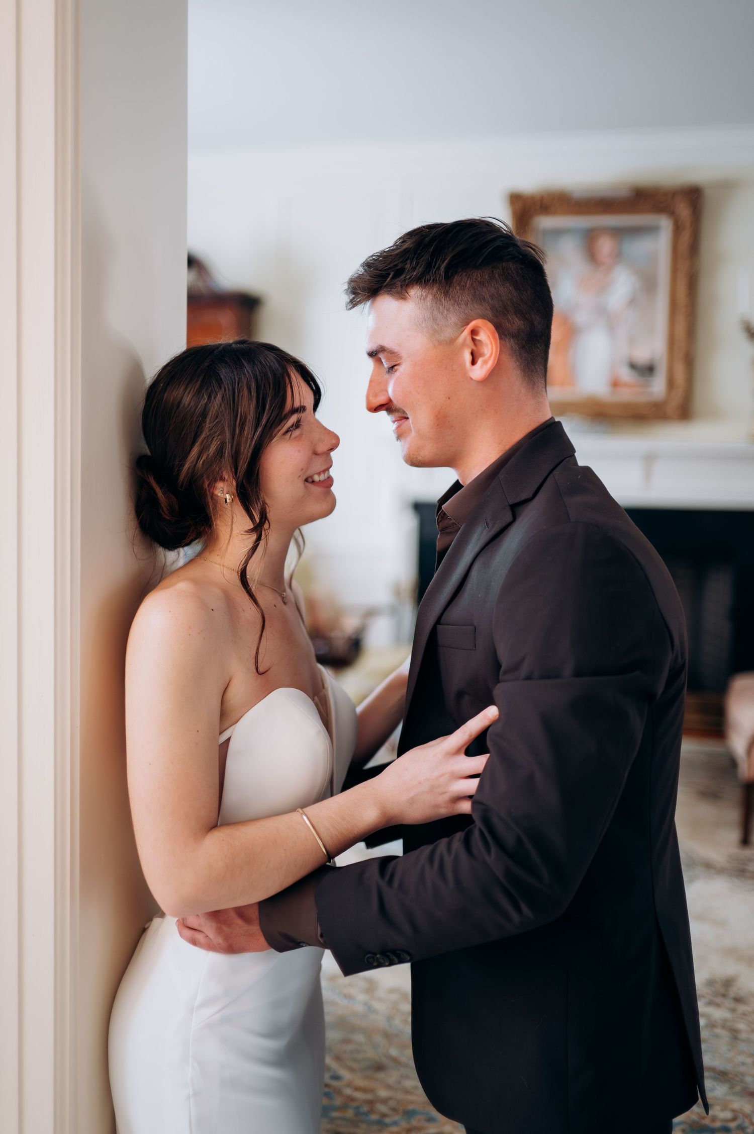 Smiling bride and groom sharing an intimate moment leaning against a column indoors.
