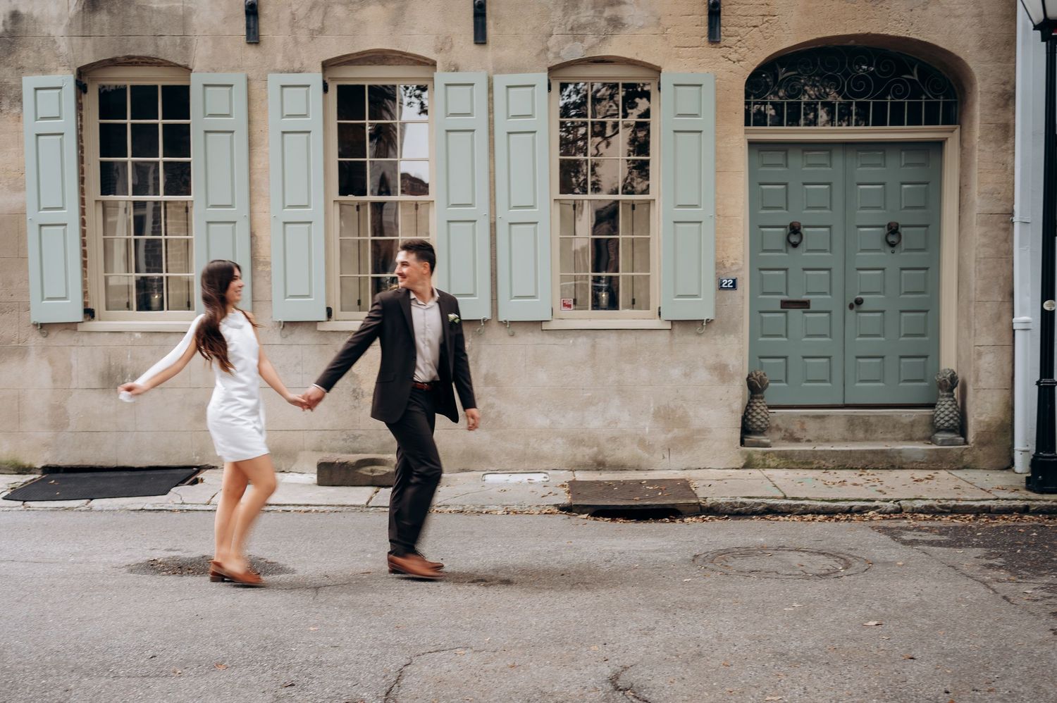 A couple walks together in a charming European alleyway with historic stone buildings and blue shutters.