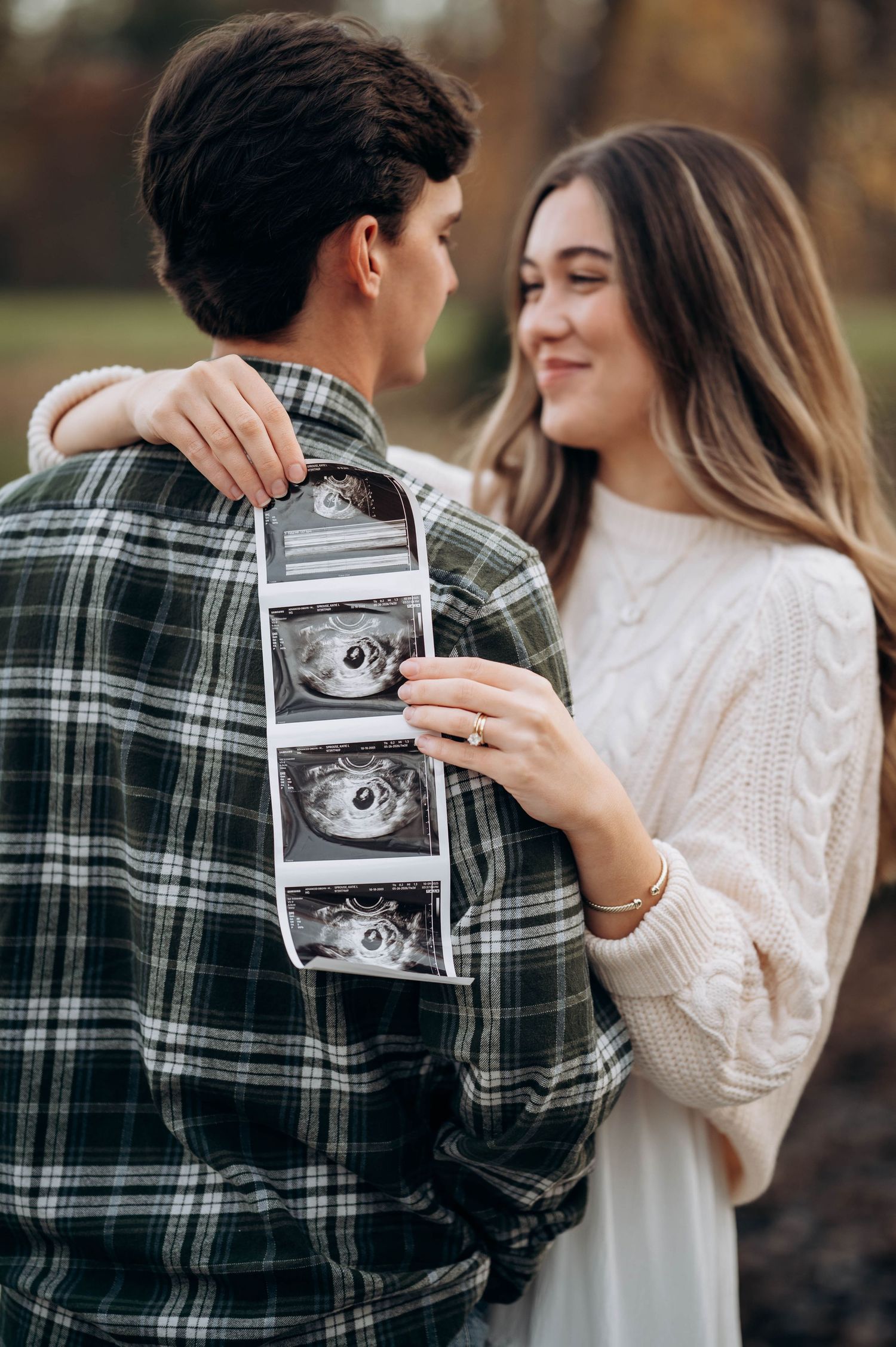 Couple holding ultrasound photos while sharing joyful moment outdoors.