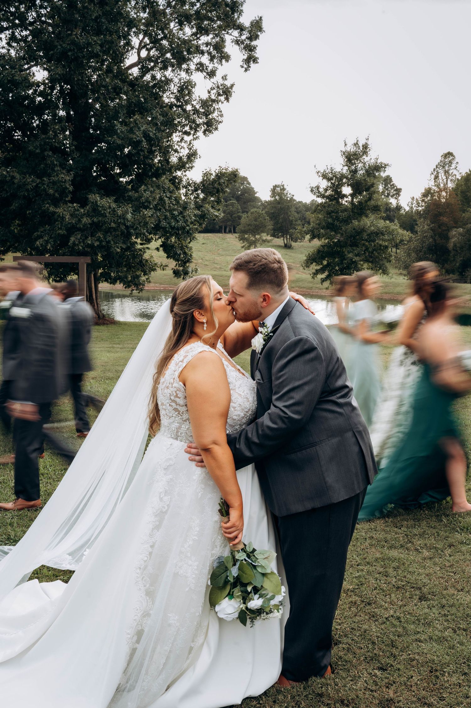 Wedding couple embraces while guests move in motion blur around them outdoors.