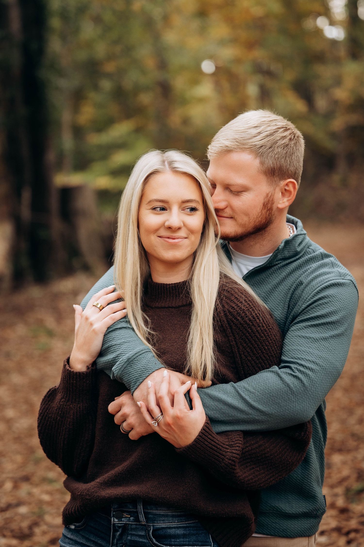 Couple in sweaters embracing during autumn photoshoot in the woods.