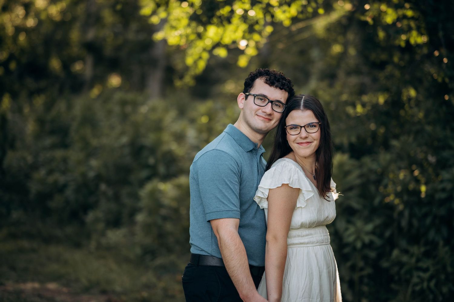 A romantic couple embraces in a sunset photoshoot by a serene lake with golden light filtering through trees.