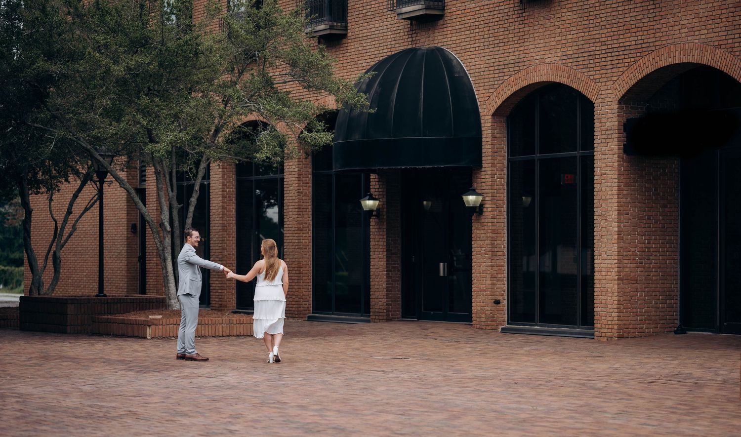 Elegant couple strolling through brick archways and columns of historic architecture.