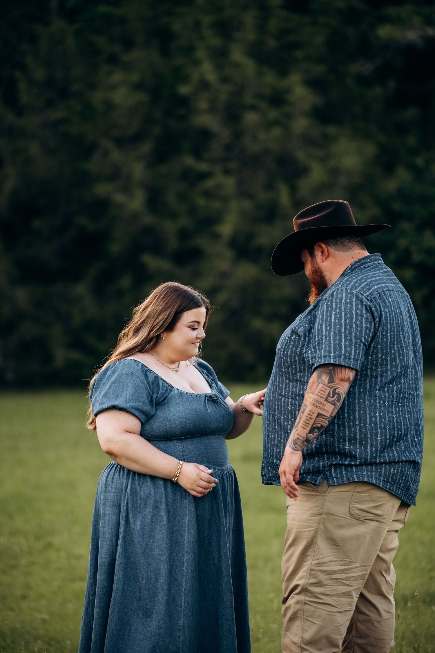 Couple sharing a romantic moment in a green field, man in cowboy hat showing woman something special.
