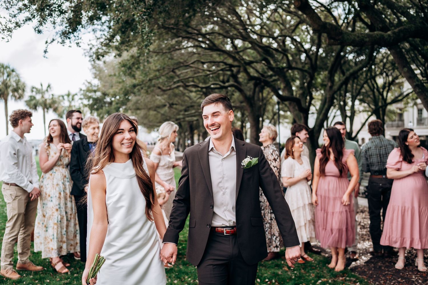 A wedding party gathers under trees with bridesmaids wearing pink dresses.