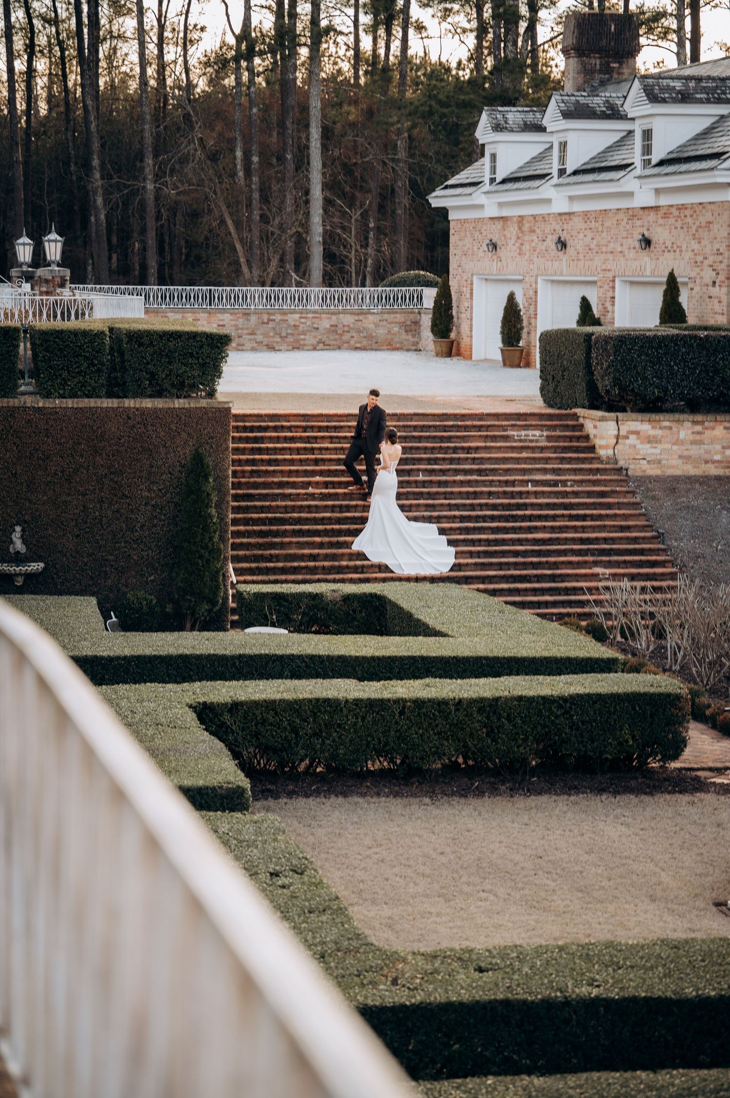 Wedding photos taken on grand brick steps leading to a white columned mansion surrounded by trees.