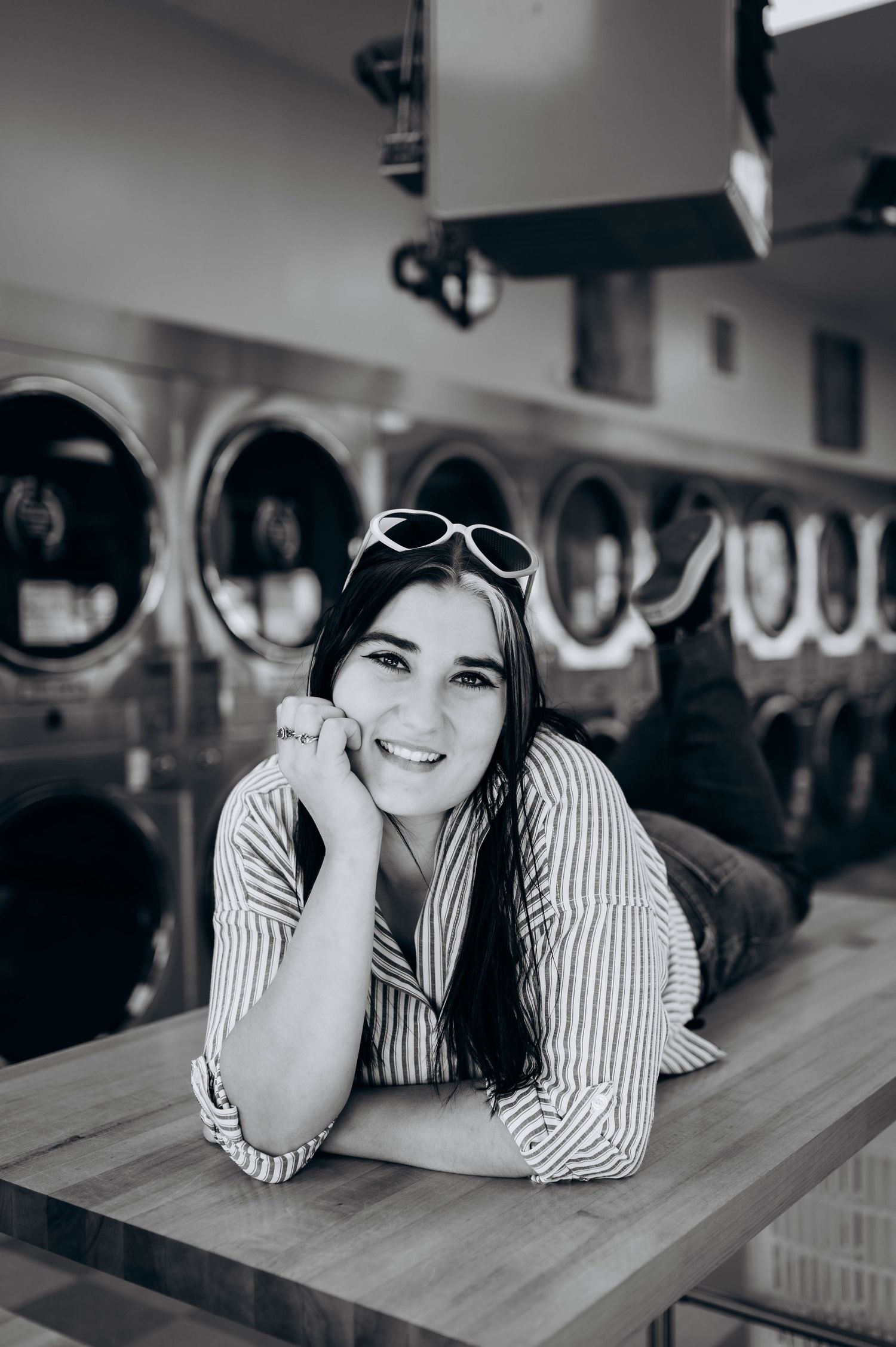 Artistic black and white portraits of someone lounging on wooden table wearing sunglasses and striped shirt.