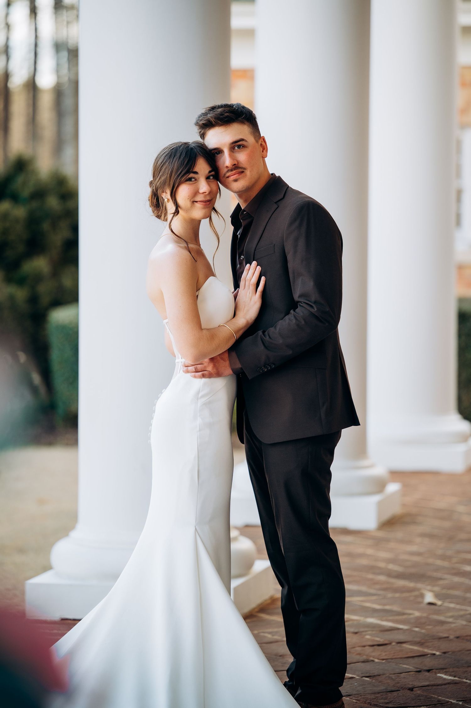 Elegant wedding portraits captured between white columns with soft natural lighting.