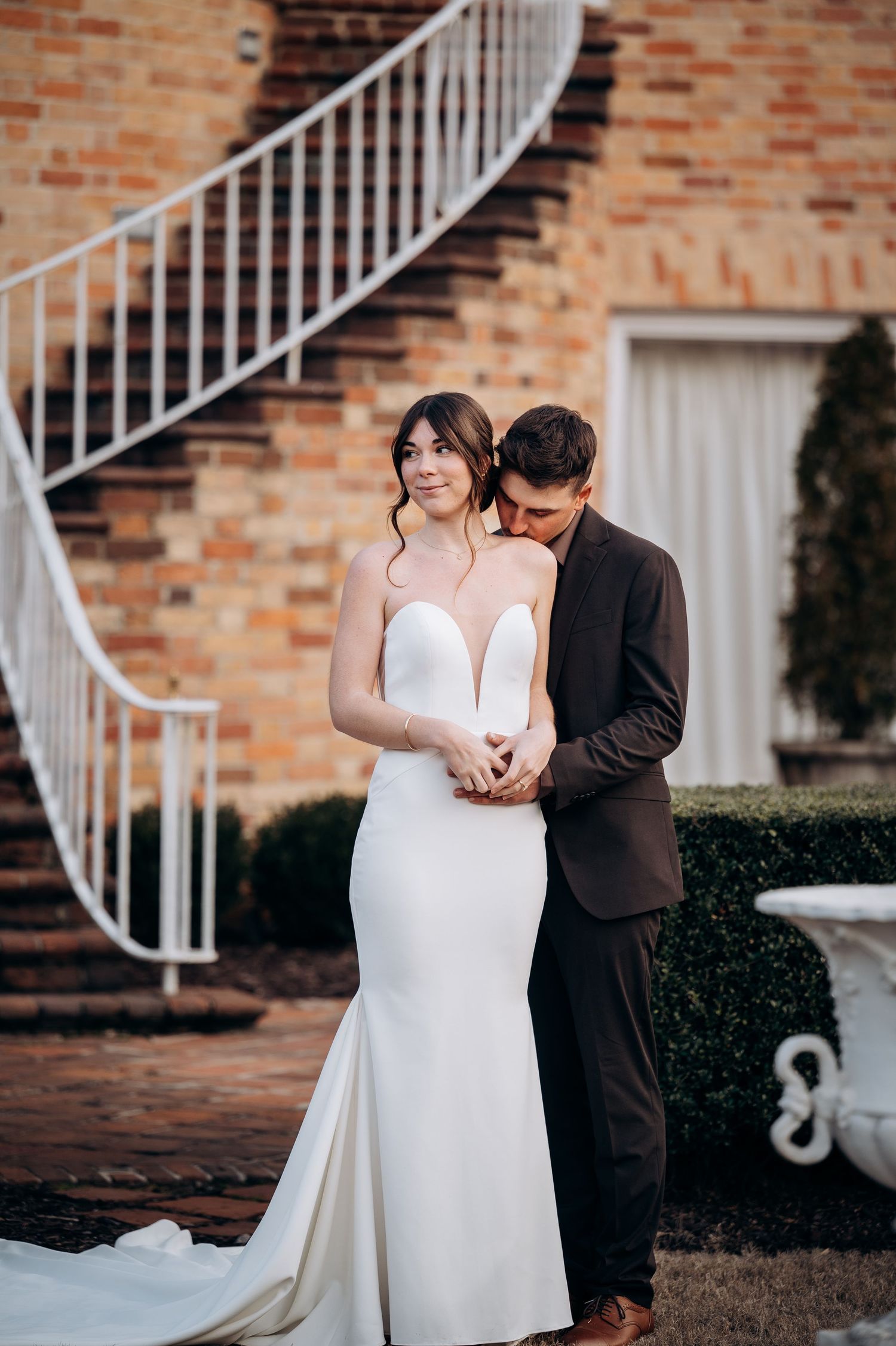 Intimate wedding portrait of newlyweds by brick staircase in formal attire.