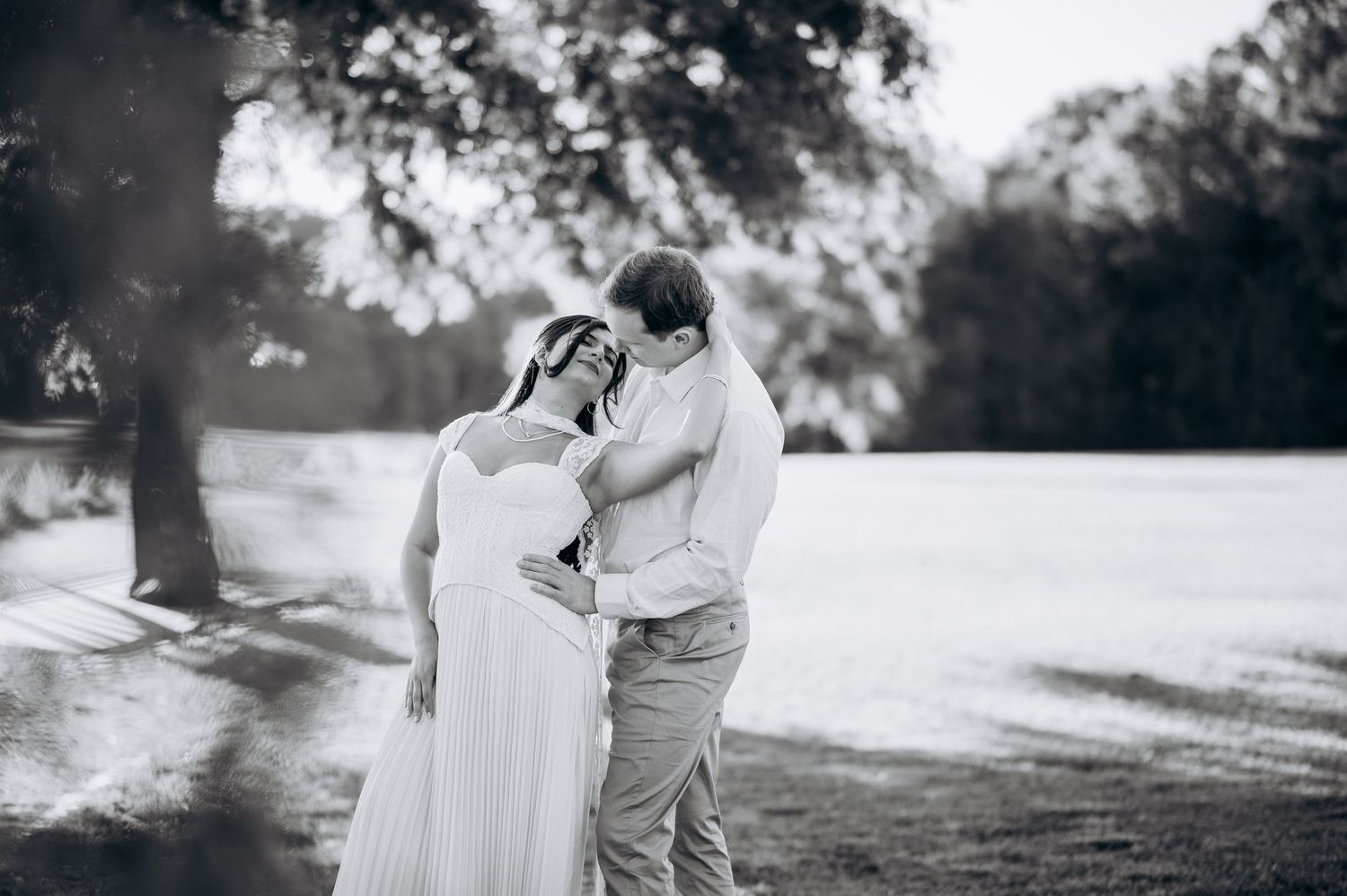 Black and white photo of a couple in wedding attire sharing a romantic moment outdoors among trees.