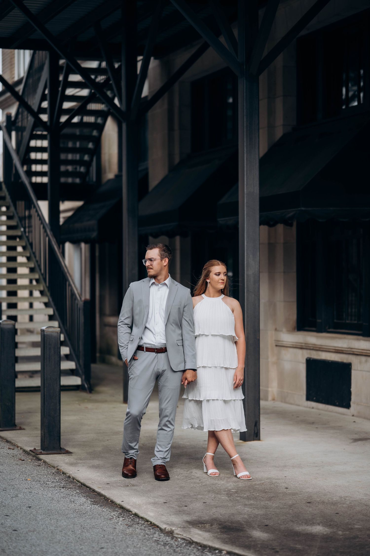 Stylish couple in grey and white outfits walking through urban covered walkway.