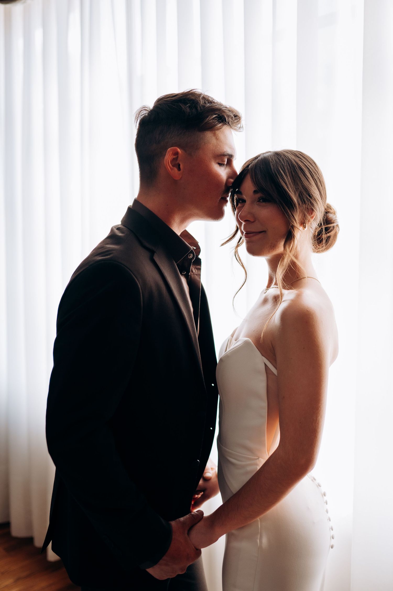 Romantic couple shares an intimate moment in front of sheer white curtains.