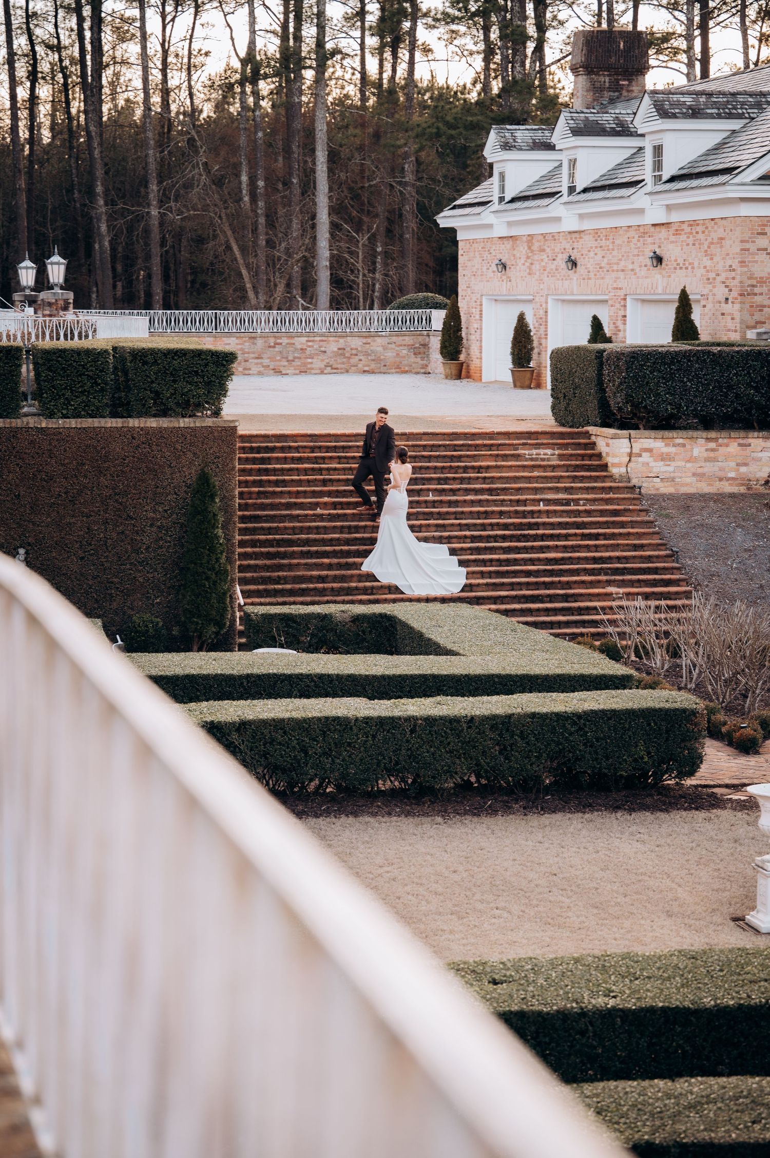 Elegant wedding venue featuring brick stairs and white architectural details surrounded by pine trees.