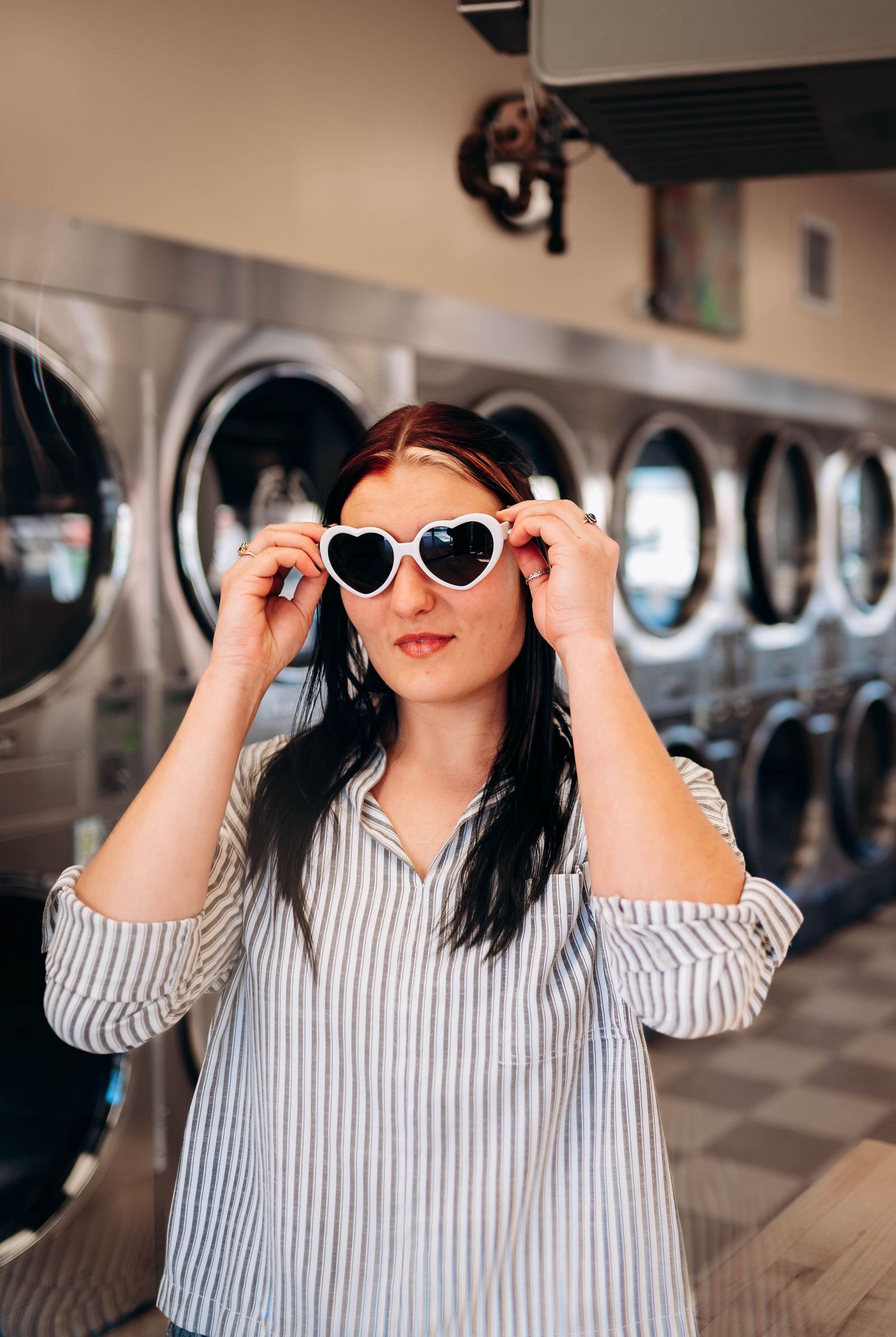 Stylish heart-shaped sunglasses and striped shirt at laundromat with washing machines in background.
