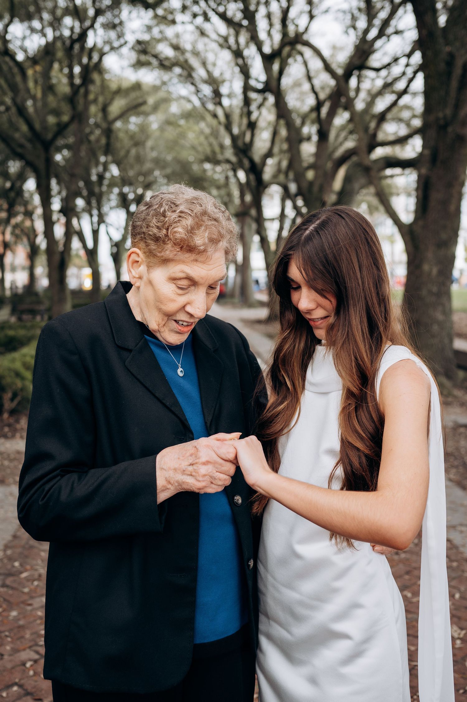 Sweet moment of ring admiration between two people in a tree-lined outdoor setting.