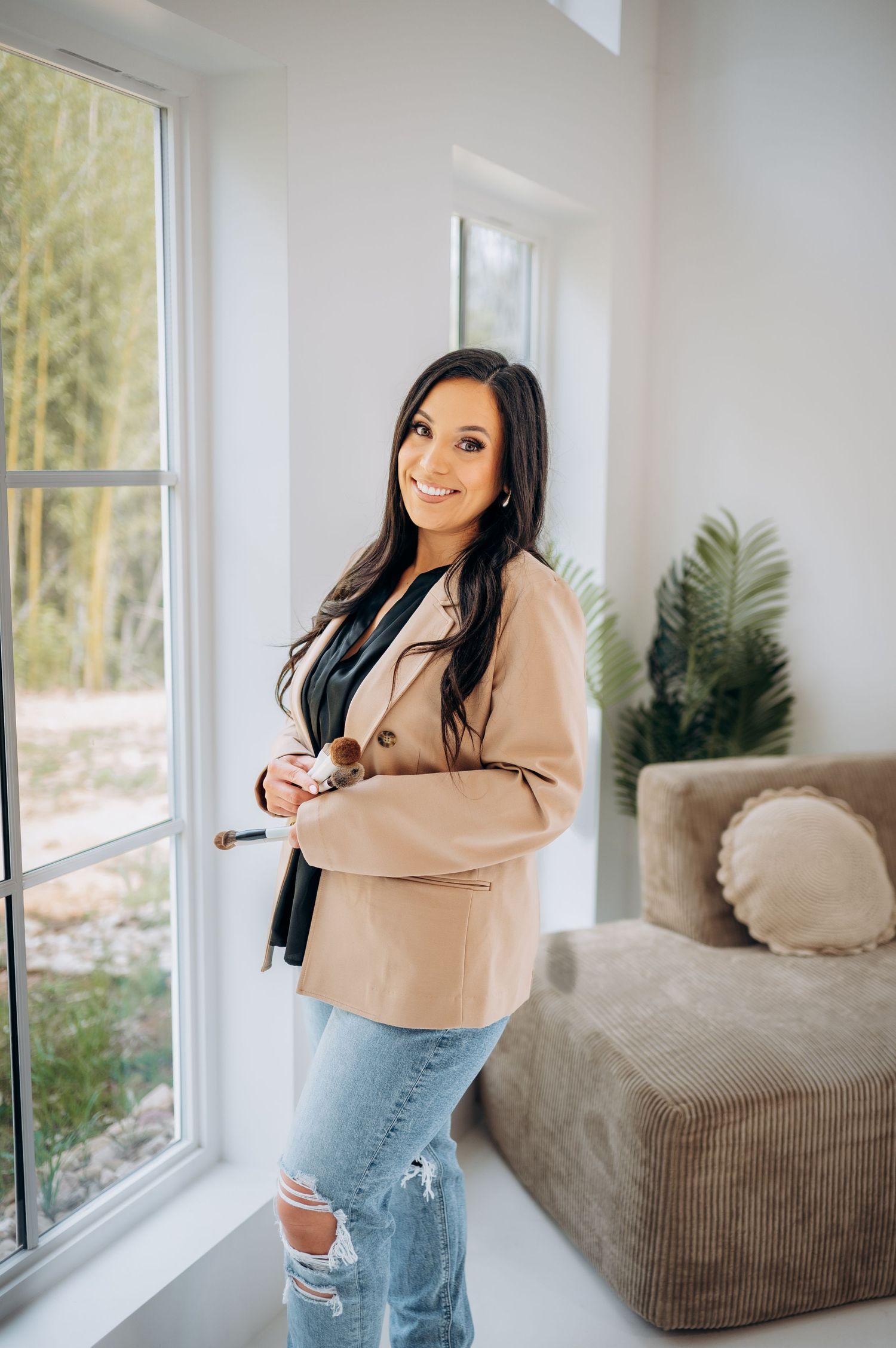 Professional lifestyle photo showing a casual business look with beige blazer and distressed jeans in bright interior.
