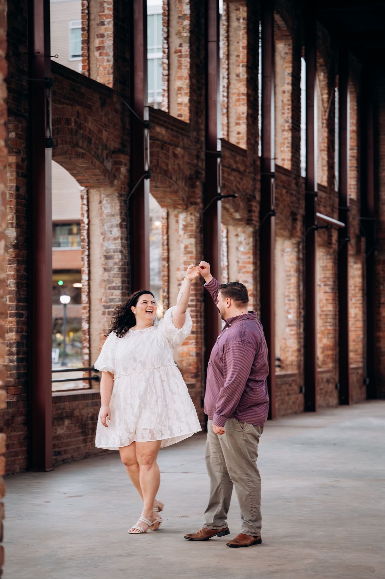 A couple shares a playful moment in a rustic brick archway corridor with natural lighting.