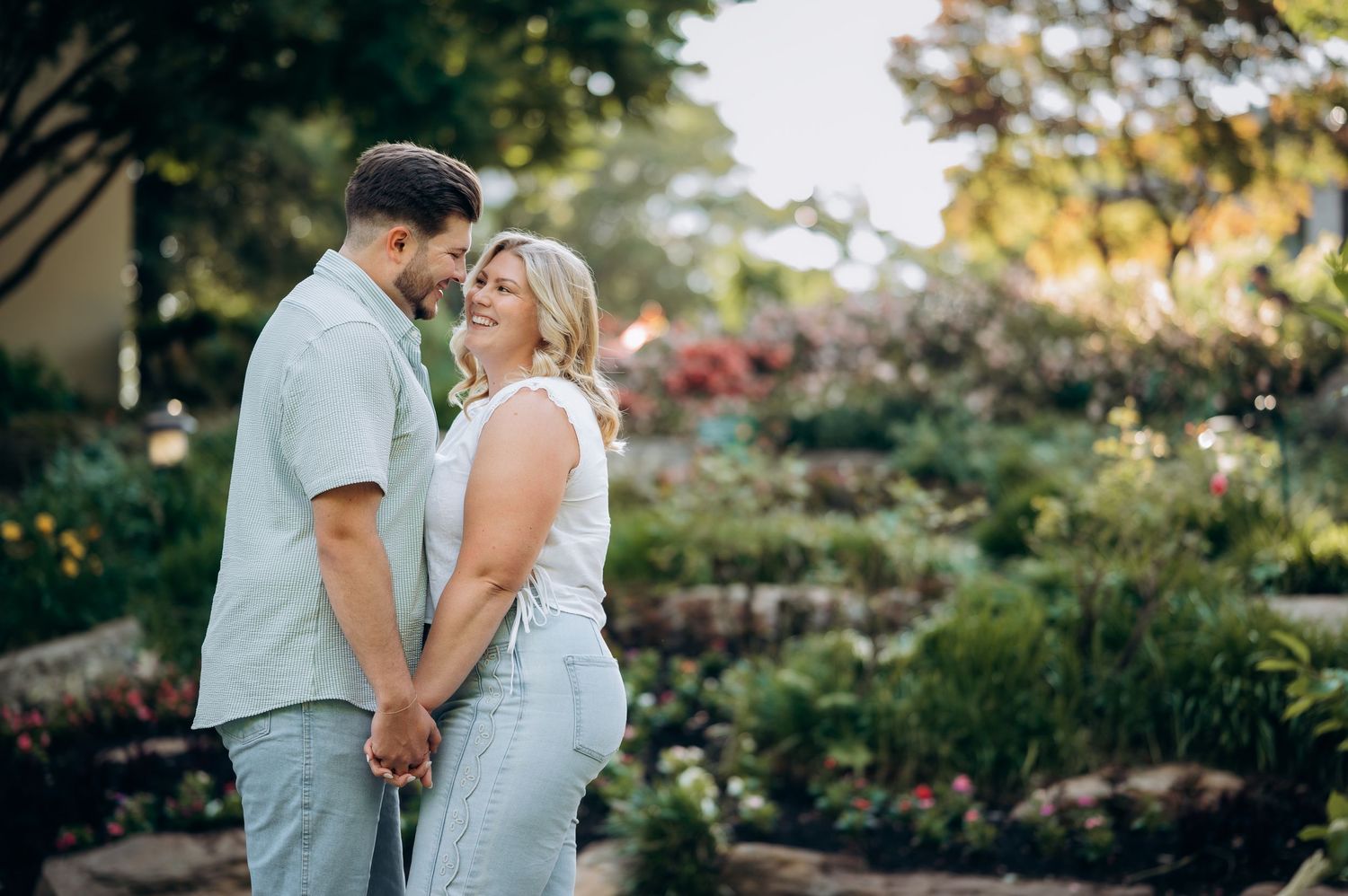 Happy couple holding hands and smiling at each other in a lush garden during golden hour.