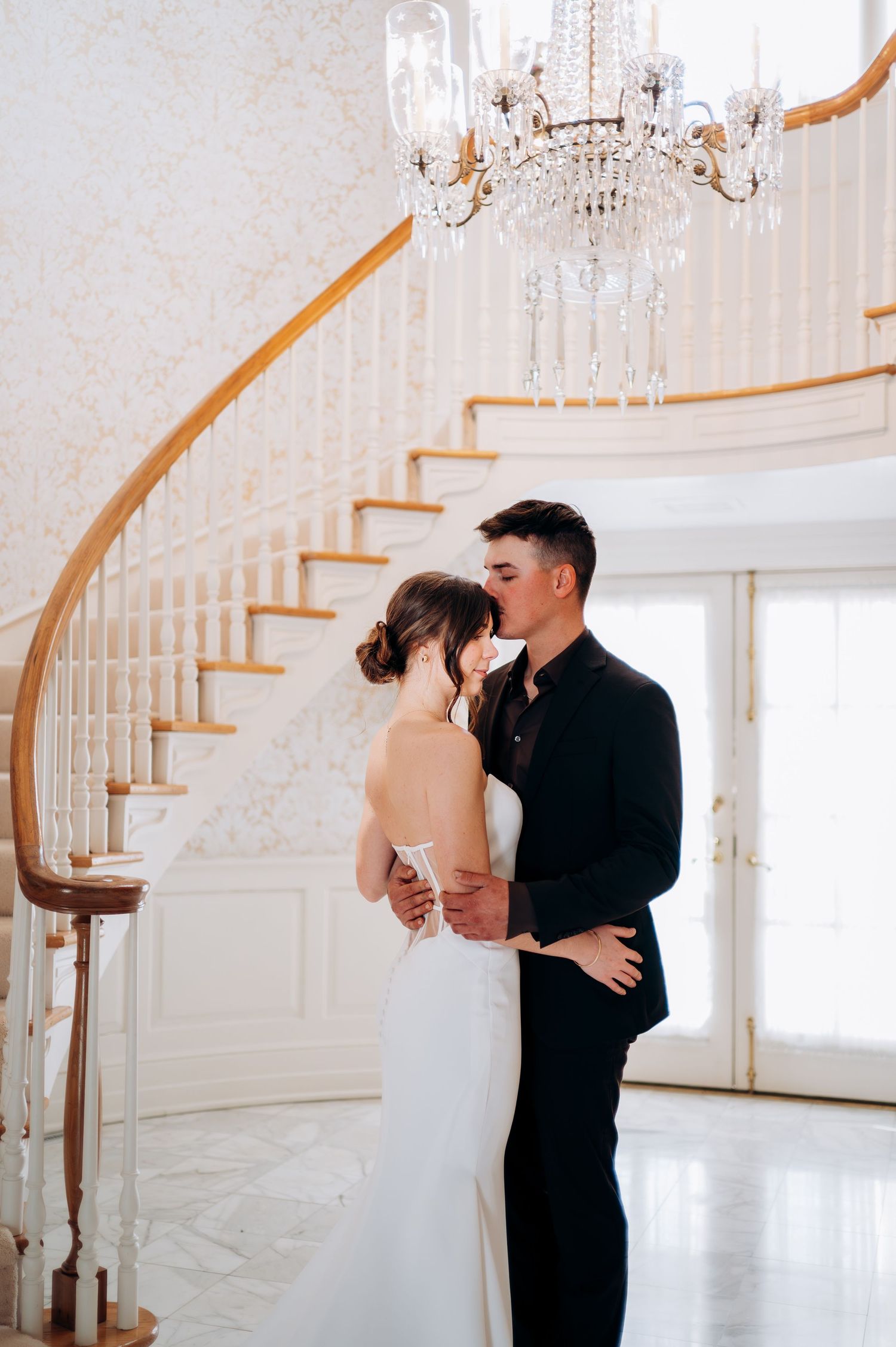 Elegant couple dancing in a bright white ballroom with a curved staircase.