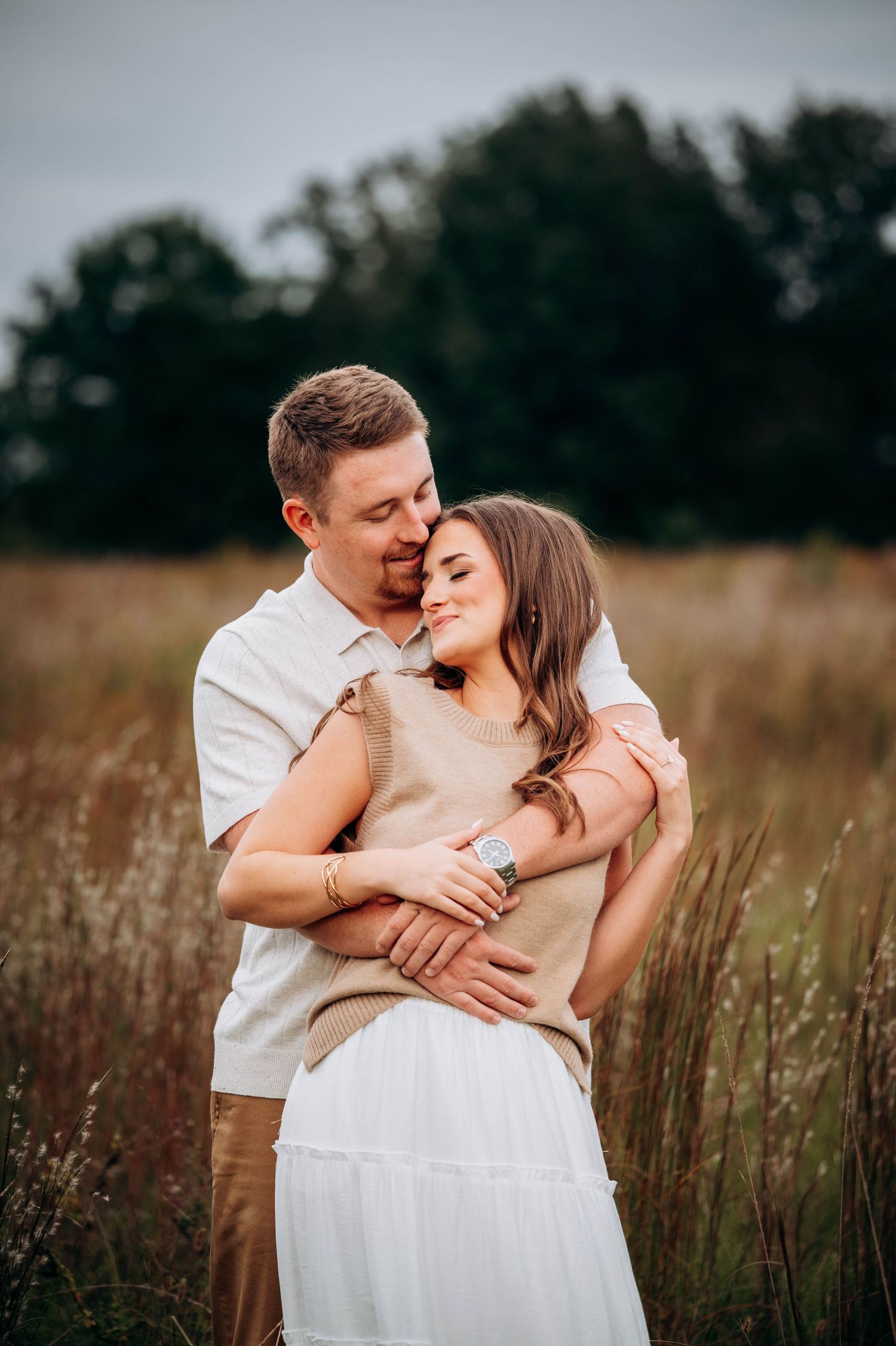 Tender embrace captured in a natural field setting with soft lighting and tall grass.