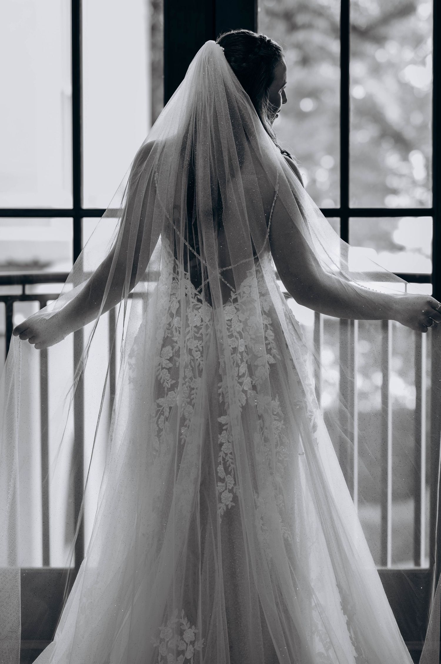 A dramatic black and white silhouette of a bride in lace gown and veil on a balcony.