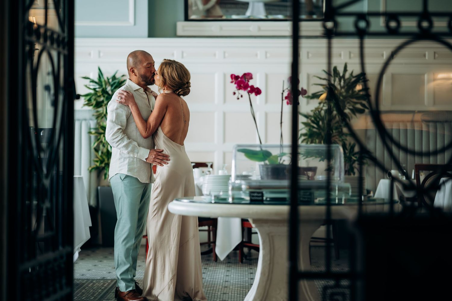 Couple sharing a romantic embrace in an elegant room with orchids and lush greenery.