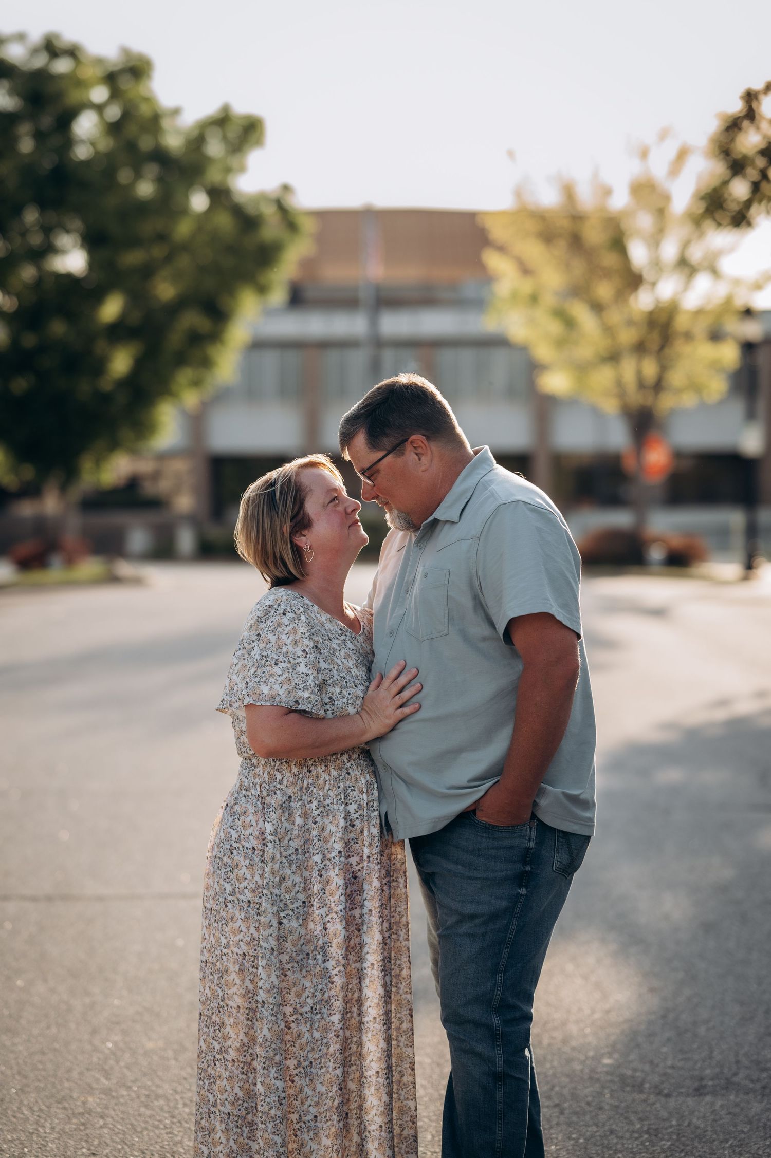 Couple sharing a romantic moment on a sunny street, woman in floral maxi dress and man in light blue shirt and jeans.