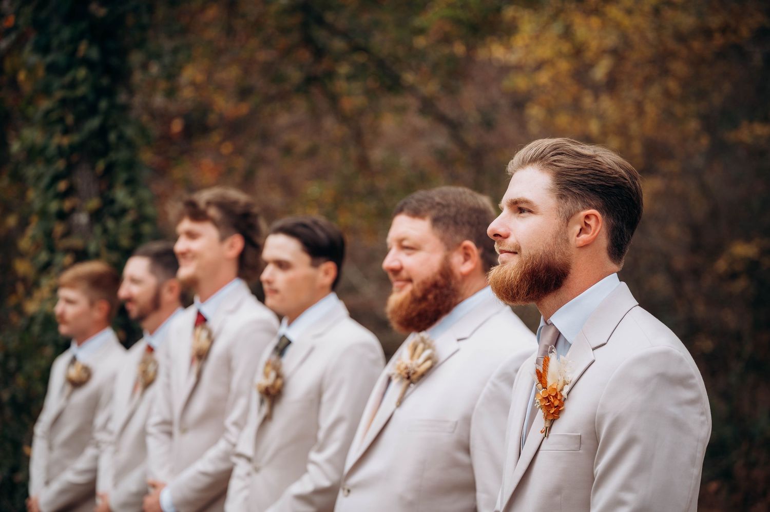 Groomsmen in light colored suits laughing together during outdoor wedding photo session.