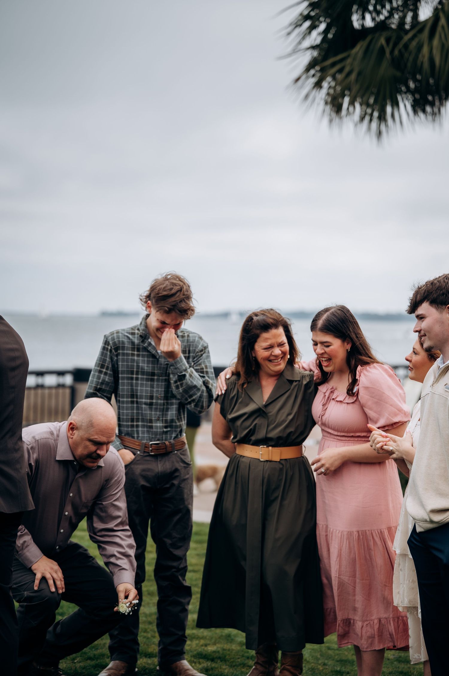 Group of friends laughing and sharing a joyful moment together outdoors near the ocean at an event.